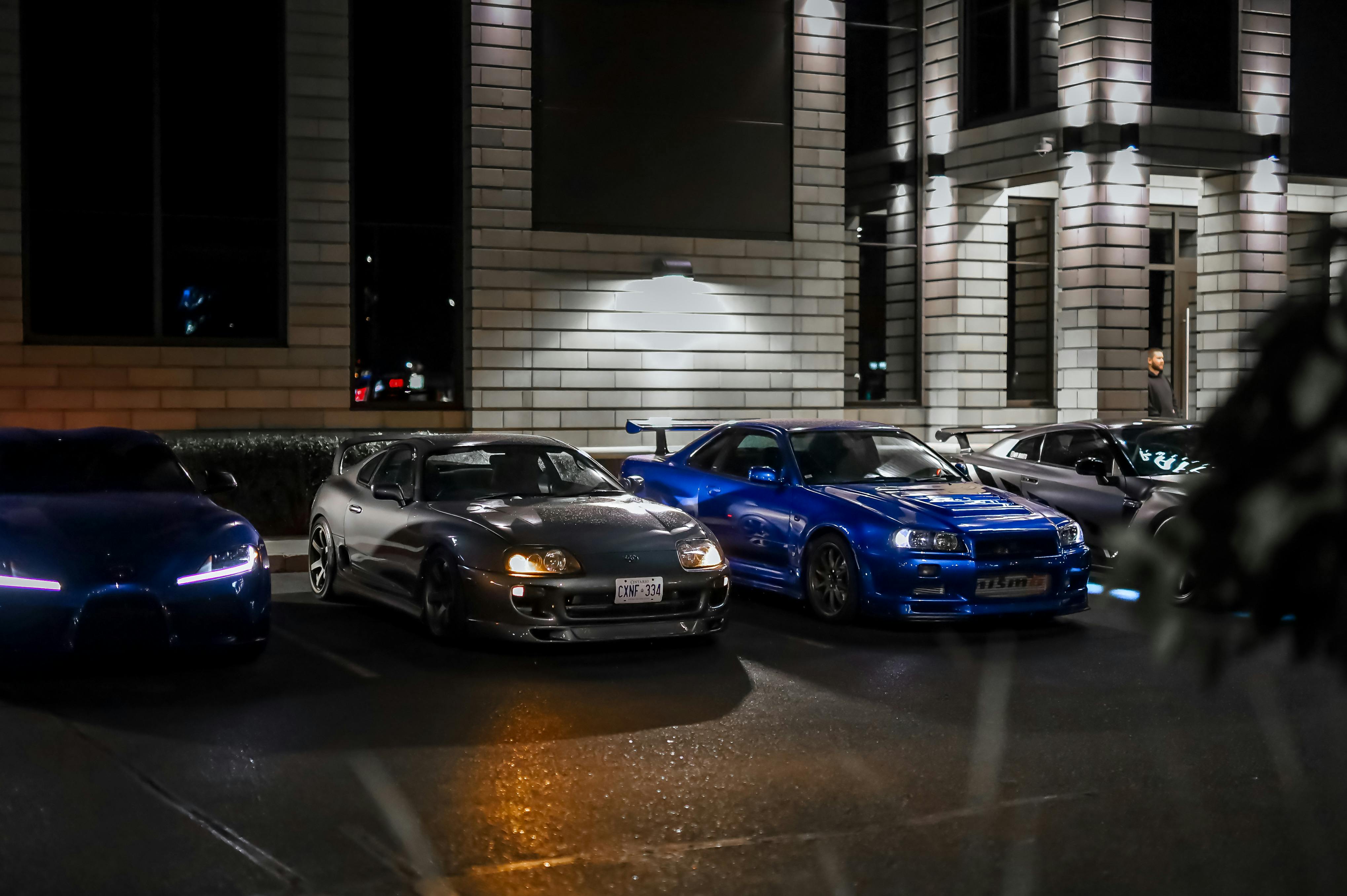 Rând de mașini într-o parcare de noapte, felinarele luminează asfaltul umed