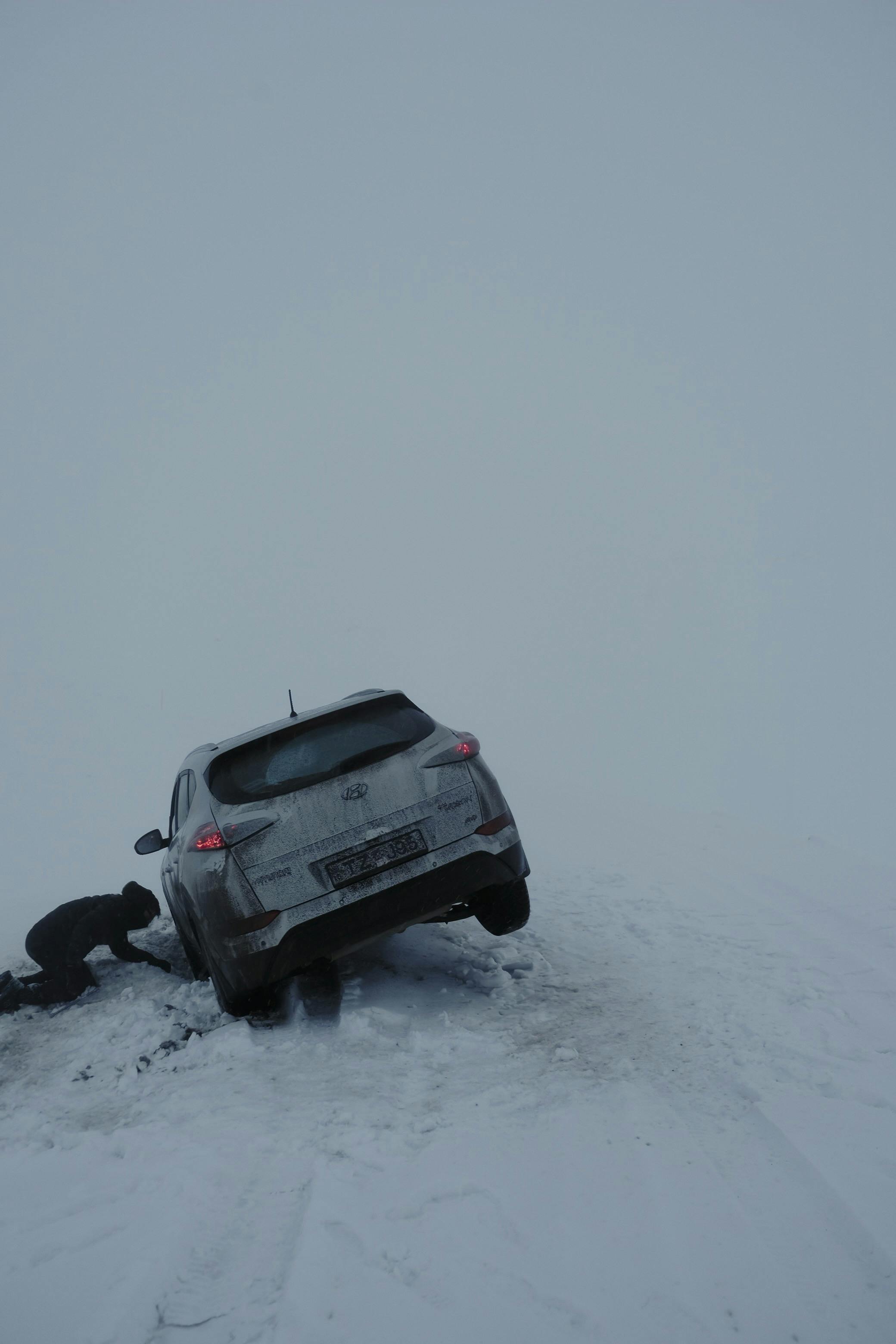 Doi oameni ajută un șofer să împingă o mașină stricată.